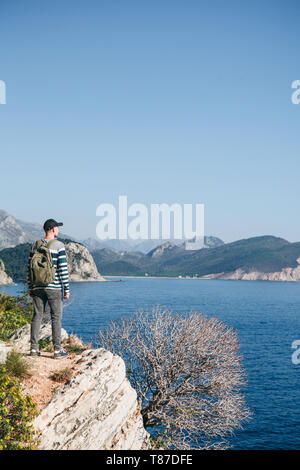 Ein Tourist mit einem Rucksack auf einer Klippe oder Hügel neben das Meer in die Ferne schaut. Allein reisen. Stockfoto