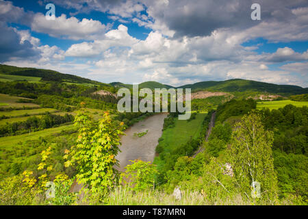 Blick vom Hügel in das Tal mit dem Fluss Berounka. Fluss Berounka, Kalksteinfelsen, Wiesen, Felder und Eisenbahn. Stockfoto