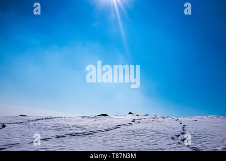 Ein schöner Berg mit Schnee bedeckt und die Spuren im Schnee auf einem blauen Himmel. Stockfoto