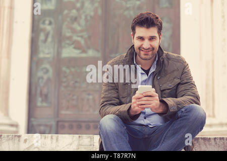 Man SMS auf ein Mobiltelefon. Casual urban professionelle Unternehmer mit Smartphone lächelt glücklich von der Kamera auf den Hintergrund der Altstadt Gebäude. Stockfoto