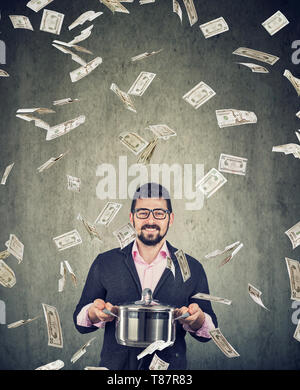 Content super aufgeregt Mann mit Kochen pan unter Geld Dollarscheine Regen auf grauen Hintergrund Stockfoto