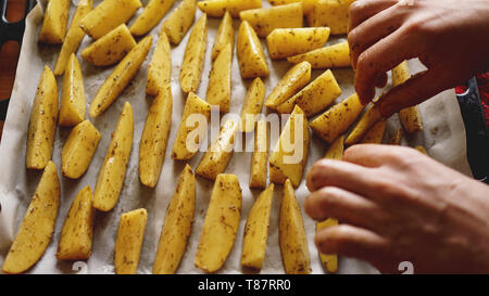 Hände - in Scheiben geschnittenen Kartoffeln auf ein Backblech mit Gewürzen und Rosmarin, Ansicht von oben, kopieren Raum Stockfoto