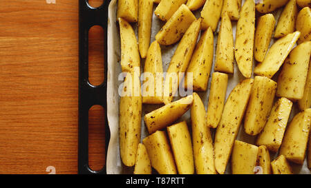 In Scheiben geschnittene Kartoffeln auf ein Backblech mit Gewürzen und Rosmarin, Ansicht von oben, kopieren Raum Stockfoto