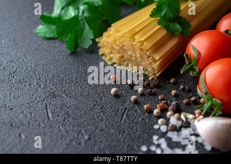 Auf einem schwarzen Hintergrund nehmen die Hälfte der Frame raw Spaghetti mit frischem Koriander Blätter, mehrere Tomaten, Knoblauchzehe, Pfeffer und grobem Meersalz Stockfoto