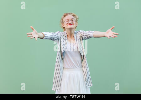 Porträt der glückliche junge blonde Frau in weißem T-Shirt, Rock, und gestreifte Bluse mit Brillen stehend mit erhobenen Armen, lächelnd und wollen zu umarmen. ind Stockfoto