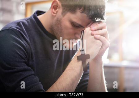 Seitenansicht der Religiösen jungen Mann mit Rosenkranz beten zu Gott zu Hause Stockfoto