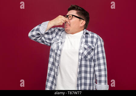 Portrait von langweilig aussehenden Mann im mittleren Alter business casual kariertem Hemd und Brille stehen und seine Nase Blockade aufgrund schlechter Geruch. Stockfoto