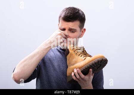 Nahaufnahme eines Menschen, die seine Nase Halten stinkenden Schuh gegen den weißen Hintergrund Stockfoto