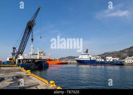 Kran Schiff Tronds Lift 6 in den Hafen von Bergen, Norwegen. AHTS Offshore Supply Vessel Insel Vanguard im Hintergrund Stockfoto