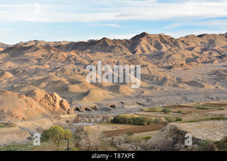 Tal unterhalb der cumbling Mud-brick Dorf Kharanaq mit antiken Aquädukt und Brücke, Seidenstraße, Iran. Stockfoto