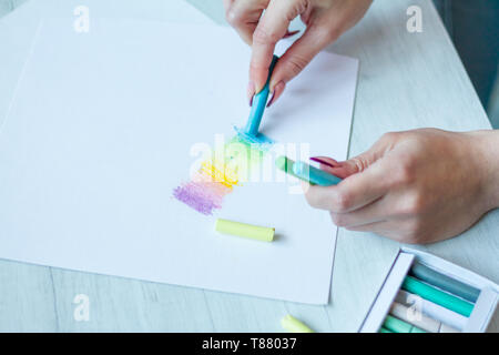 Nahaufnahme Blick von oben auf die weibliche Hände zeichnen mit bunten Pastellkreiden auf einem weißen Blatt, eine Schachtel mit Buntstiften in der Nähe stehen, Hintergrund oder Konzept Stockfoto