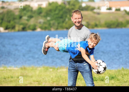 Gerne Vater und Sohn mit Fußball spielen in der Nähe von Fluss Stockfoto