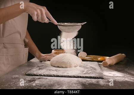 Frau sichten Mehl auf den Teig gegen den dunklen Hintergrund Stockfoto