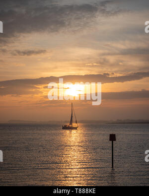 Ein Segelboot silhouette Segeln vorbei an den Sonnenaufgang auf das ruhige Meer Stockfoto