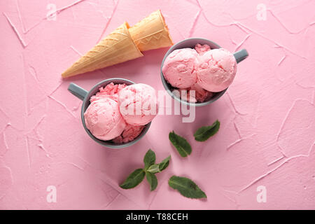 Tassen mit leckeren Erdbeer Eis auf Farbe strukturierten Hintergrund Stockfoto