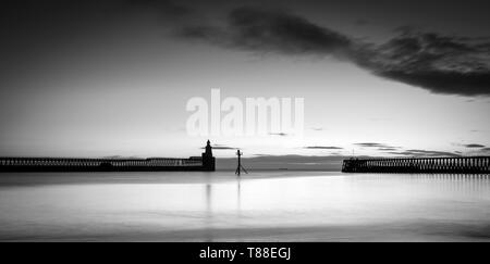 Frühen kalten Wintermorgen die orange Sunrise, die Silhouetten der Blyth port Piers & Hafen Leuchtturm in Northumberland zu fangen Stockfoto