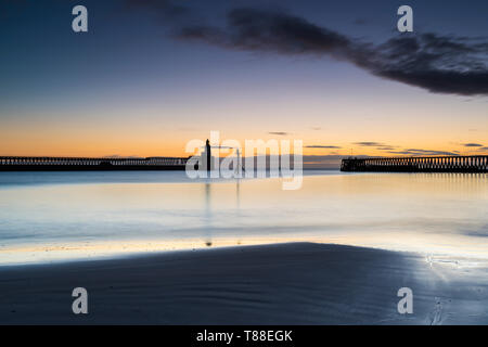 Frühen kalten Wintermorgen die orange Sunrise, die Silhouetten der Blyth port Piers & Hafen Leuchtturm in Northumberland zu fangen Stockfoto