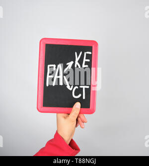 Weibliche Hand, die Kreide Rahmen mit Kreide Inschrift fake und tat, grauer Hintergrund Stockfoto