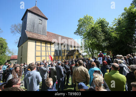 Larz, Deutschland. 12. Mai 2019. Die Teilnehmer einer Kundgebung für den Erhalt der Kultur und Musik Festival 'Fusion' stand vor der Kirche von lärz. Rund 100 Menschen protestierten am Sonntag in Lärz (Mecklenburger Seenplatte) gegen eine Polizeiwache und Polizeistreifen auf die Alternative "Fusion" Festival. Quelle: dpa Picture alliance/Alamy leben Nachrichten Stockfoto