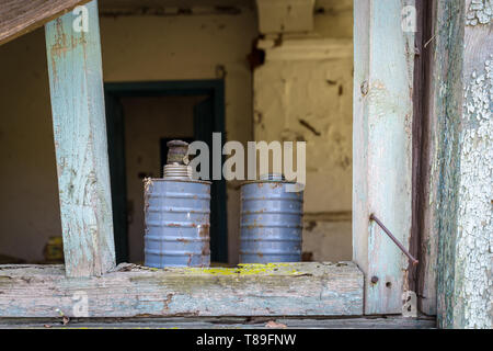 Zwei Dosen aus Metall hinter einem Fenster mit Glasscherben von einem alten, verlassenen Haus in Belarus Sperrzone von Tschernobyl in Weißrussland Stockfoto