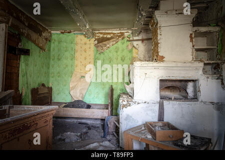 Interieur mit Ofen und Bett in einem verlassenen kleinen Haus in Weißrussland Tschernobyl Sperrzone, die vor kurzem für die Öffentlichkeit geöffnet von April 2019. Stockfoto