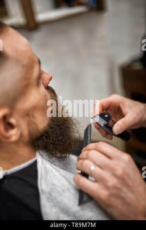 Seitenansicht des Ernteguts männliche Gesicht im Friseursalon schneiden roten Bart und Friseur hand Haarschneider Stockfoto