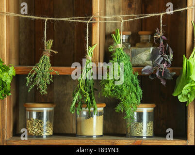 Frische Kräuter hängen an String gegen Holzfachböden Stockfoto