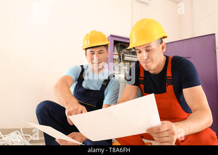 Zwei Elektriker mit Haus Plan in der Nähe der Verteilung im Innenbereich Stockfoto