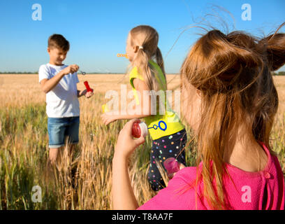 Süße kleine Kinder bläst Seifenblasen im weizenfeld an einem sonnigen Tag Stockfoto