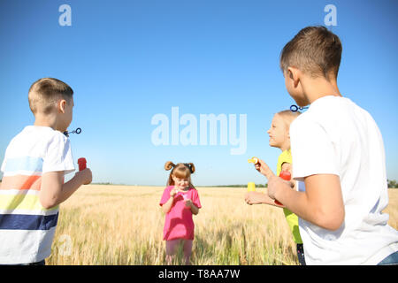 Süße kleine Kinder bläst Seifenblasen im weizenfeld an einem sonnigen Tag Stockfoto