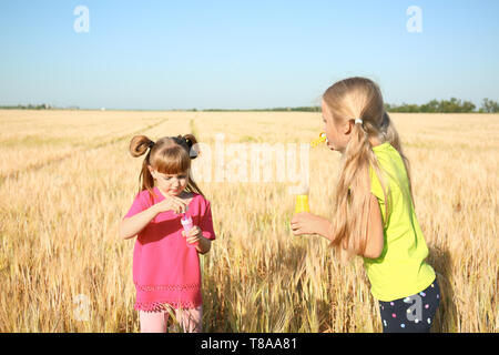 Süße kleine Mädchen bläst Seifenblasen im weizenfeld an einem sonnigen Tag Stockfoto