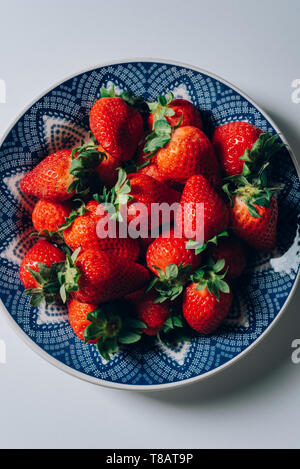 Frische reife Erdbeeren in eine blaue und weiße Platte, auf der weißen Tisch Stockfoto