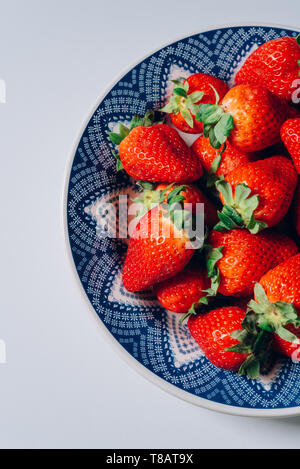 Frische reife Erdbeeren in eine blaue und weiße Platte, auf der weißen Tisch Stockfoto