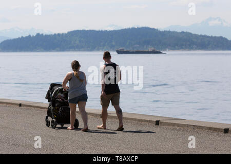 Seattle, Washington: Ein junges Paar Spaziergänge entlang Alki Trail in West Seattle als die Stadt stellt rekordverdächtige Wärme für den zweiten Tag in Folge. Stockfoto