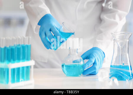 Wissenschaftler gießen Farbe Flüssigkeit in Kolben im Labor Stockfoto