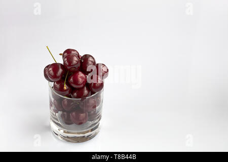 Reif und roten Kirschen in einem Glas auf einem hellen Hintergrund angeordnet, ein Bild in einem high key Stockfoto