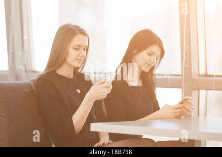 Mitarbeiter können Sie über Ihr Smartphone an einem Tisch in einem Cafe sitzen. Mensch und Technik Stockfoto