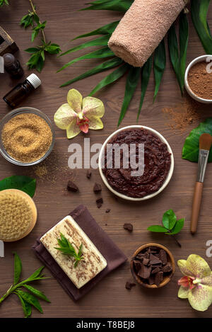 Schokolade Spa Komposition mit Pflanzen und Blumen, flach. Natural Spa Schokolade kosmetische Produkte und Behandlung organischer Konzept auf dunklem Holz zurück Stockfoto