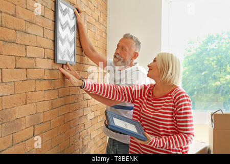 Reifes Paar hängende Bild an der Wand im Innenbereich. Umzug in neues Haus Stockfoto