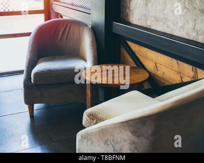 Vintage Stoff Sessel mit runden Holztisch in der Nähe der Wand, Beton, Stahl und Holz- wand im Cafe. Stockfoto