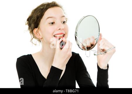 Teenaged Mädchen im schwarzen Kleid, die im Mirror Make-Anwendung Lippenstift - Weißer Hintergrund Stockfoto