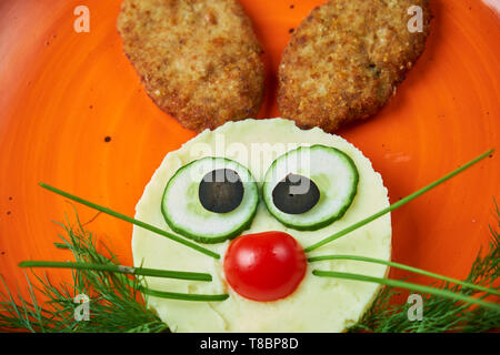 Menü für Kinder, Schnitzel mit Kartoffelbrei in Form eines Hasen Kopf auf einem orange Platte auf grauem Hintergrund Stockfoto