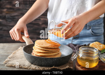 Frau gießen Honig auf leckere Pfannkuchen an den hölzernen Tisch Stockfoto