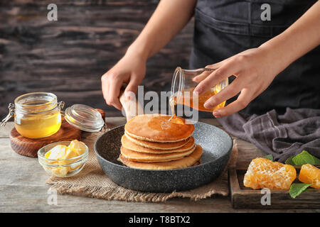 Frau gießen Honig auf leckere Pfannkuchen an den hölzernen Tisch Stockfoto