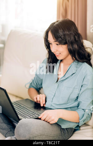 Menschen, Freizeit und Technik. Freudige dunkelhaarige Dame mit Laptop zu Hause ausruhen. Indoor Portrait von Gerne jungen kaukasischen Frau auf Posing Stockfoto