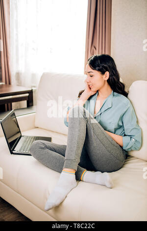 Junge brünette Frau mit blauen Shirt, grau Leggings sitzen mit überraschten Ausdruck und hält Ihr Gesicht beim Lesen einige außergewöhnliche Nachrichten, rece Stockfoto