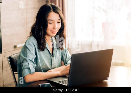 Schwere jungen kaukasischen weibliche Unternehmer Gespräch am Handy und Arbeiten am Laptop sitzen am Tisch in ihrem Home Office. Freelancer, Trainin Stockfoto