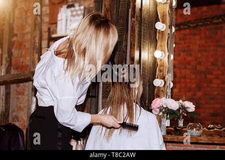 Friseur trocknen Blonde weibliche Haar mit professioneller Haartrockner im Beauty Salon. Nahaufnahme von Hairstylist mit Haarbürste und Haartrockner. Stockfoto