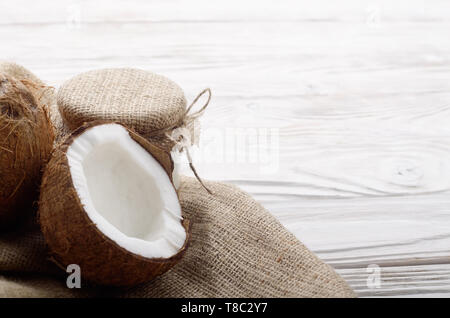 Coconut Shell mit Fleisch auf Hanf Sack auf weißen Küche aus Holz Tisch Stockfoto