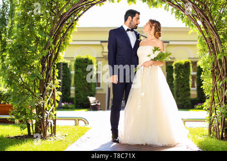 Happy Hochzeit paar unter Blumen Bogen im Freien Stockfoto